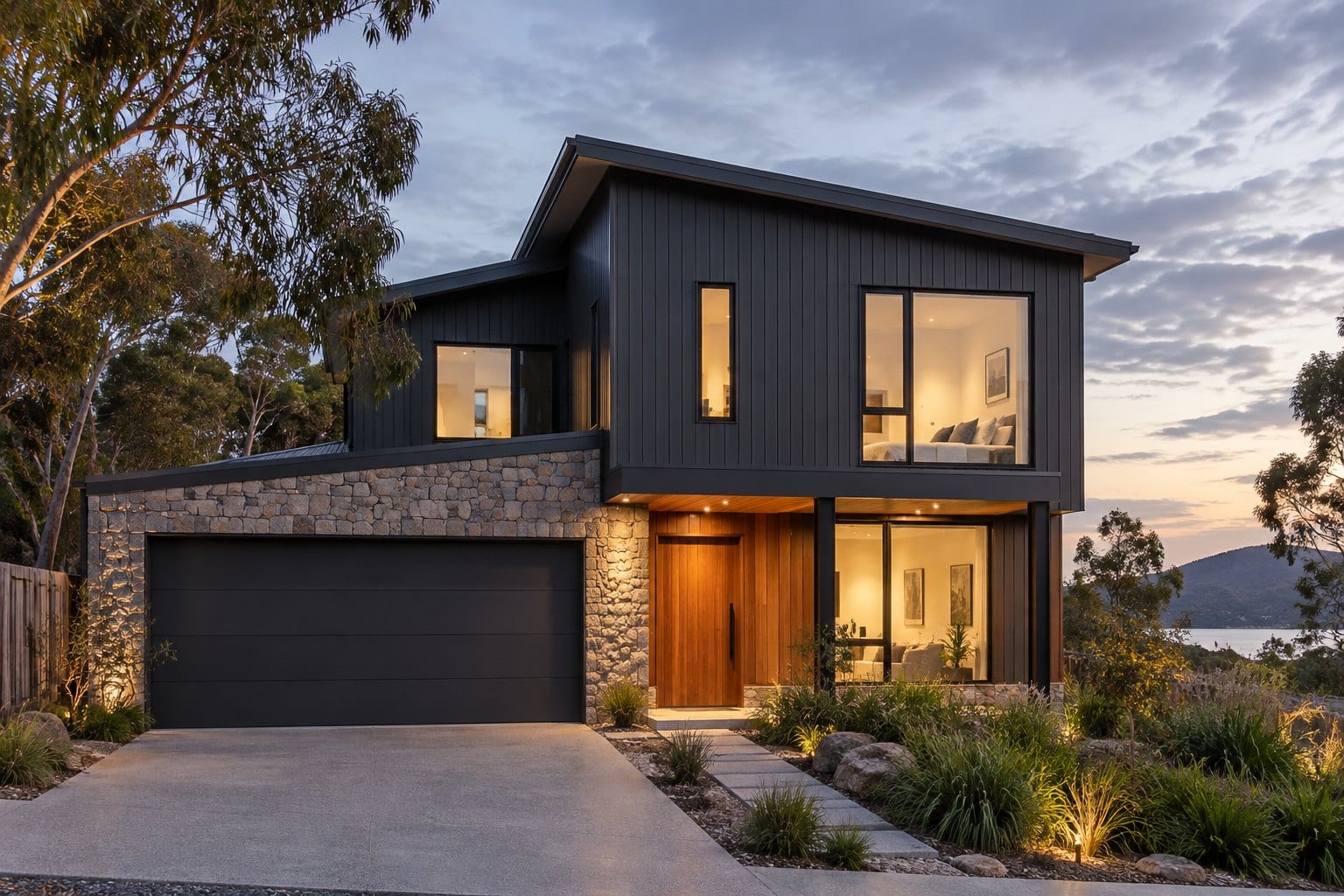 A two-storey home with dark vertical cladding, a stone-clad garage and a timber entry door at dusk